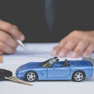 toco vehicle service contracts provider good man in black suit signing paper contract blue toy car  car keys pocket calculator in front of him on white table